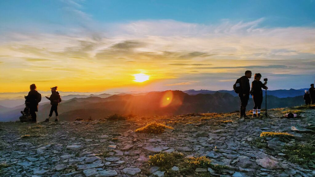 Hikers silhouette against a vibrant sunset on a mountain peak, capturing the stunning view with cameras, blending adventure with nature's beauty.