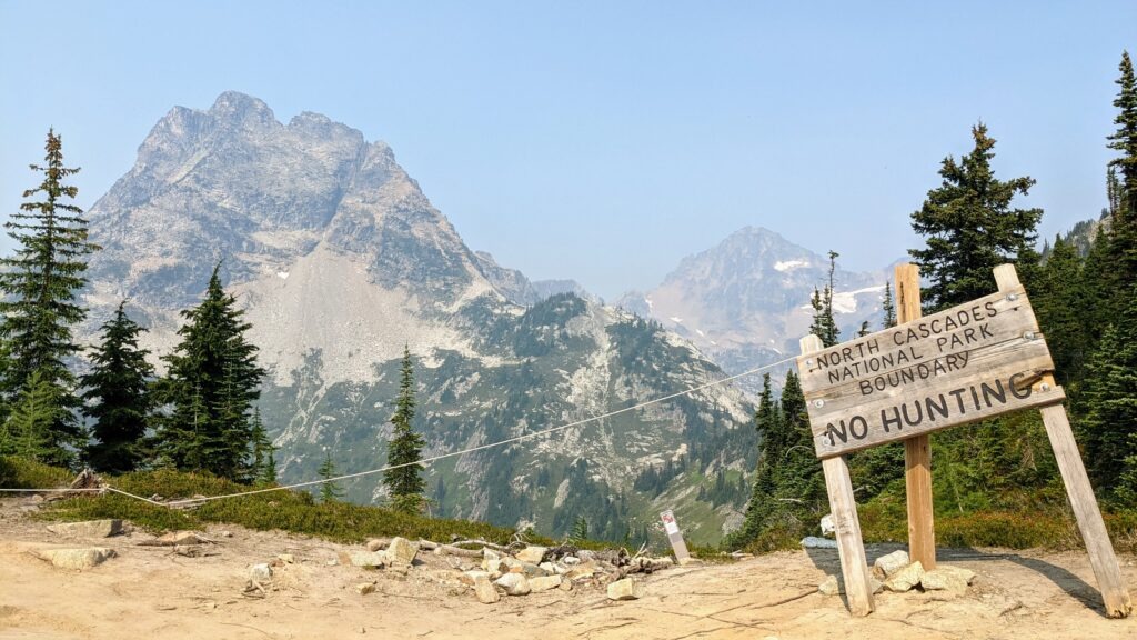 North Cascades National Park boundary sign with mountains in the background. It states "No Hunting," emphasizing park regulations and conservation efforts.