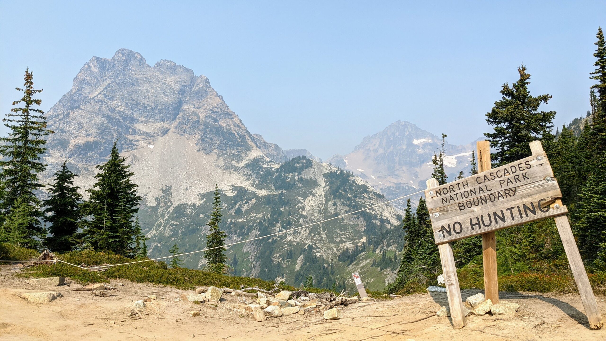 North Cascades National Park boundary sign with mountains in the background. It states "No Hunting," emphasizing park regulations and conservation efforts.