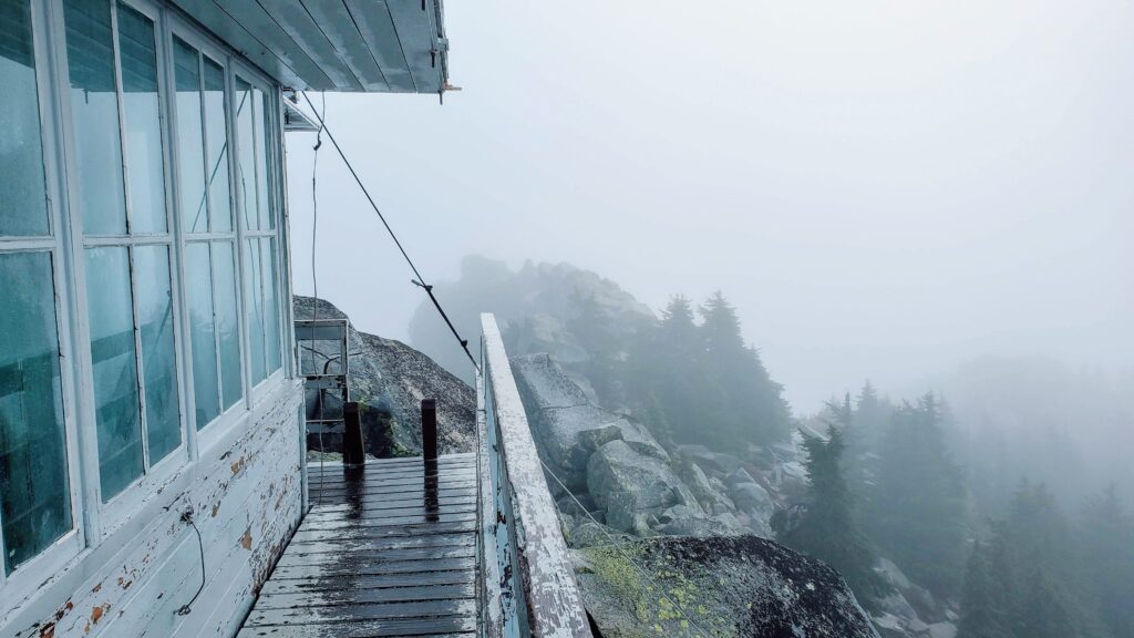Wooden deck of a weathered lookout tower, overlooking a misty landscape filled with trees and rocks. A serene, isolated scene conveying nature's beauty.