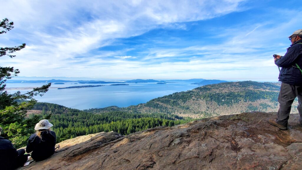 Hikers enjoy a scenic viewpoint overlooking islands and forests under a blue sky, capturing the beauty of nature during their adventure.