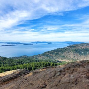 Hikers enjoy a scenic viewpoint overlooking islands and forests under a blue sky, capturing the beauty of nature during their adventure.