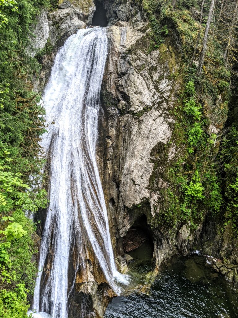 Majestic waterfall cascading over rocky cliffs into a serene pool, surrounded by lush greenery and forest, highlighting natural beauty and tranquility.