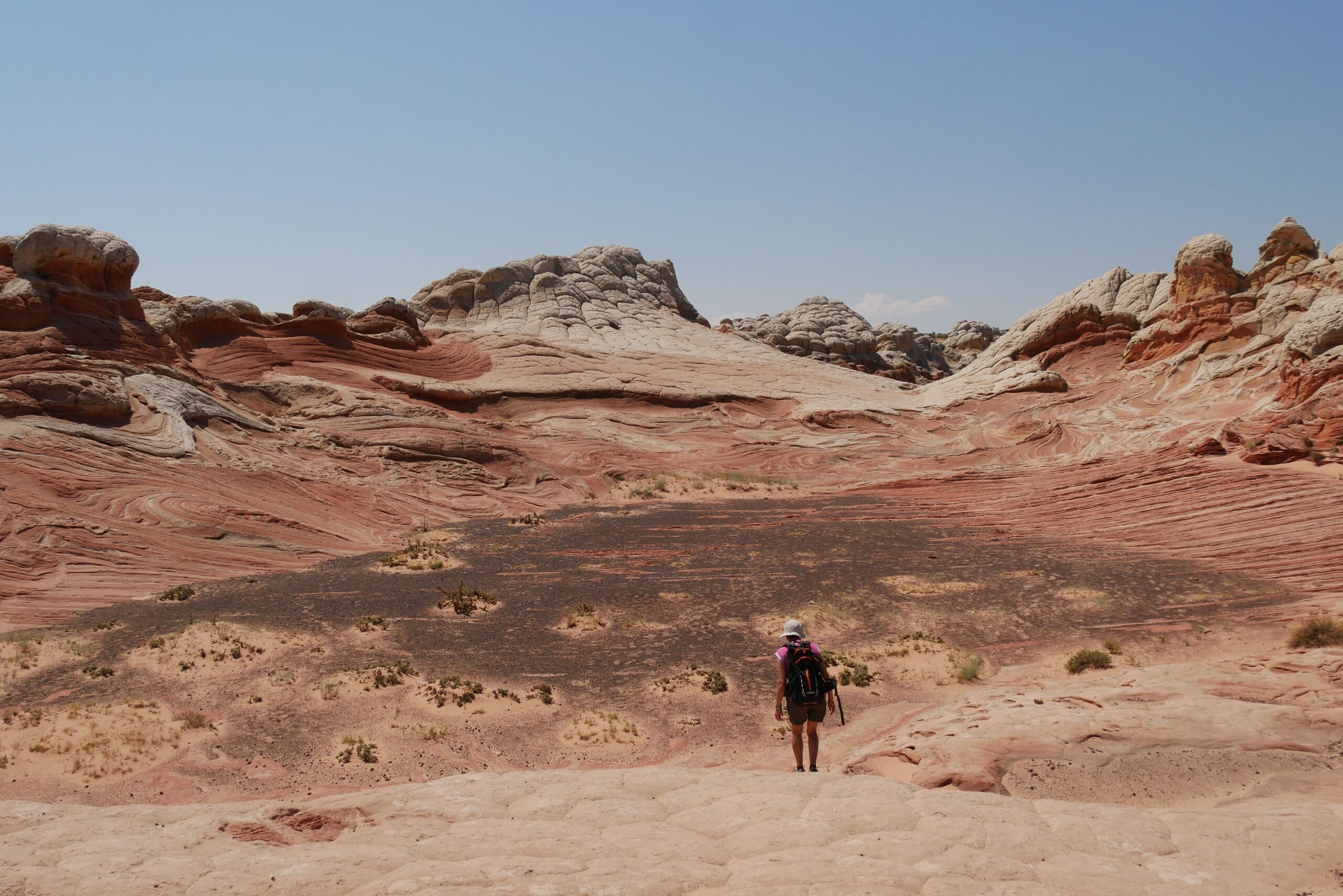 A lone traveler exploring the vibrant rock formations in a desert landscape under clear skies.
